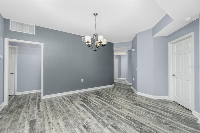 unfurnished room featuring a notable chandelier, wood finished floors, visible vents, and baseboards