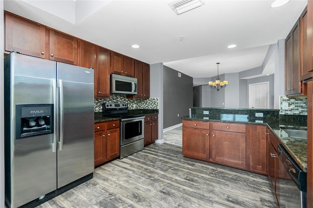 kitchen featuring visible vents, a peninsula, stainless steel appliances, light wood-style floors, and tasteful backsplash