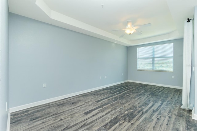 unfurnished room featuring a tray ceiling, a ceiling fan, baseboards, and dark wood-style flooring