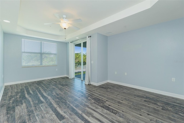 empty room with ceiling fan, a tray ceiling, baseboards, and dark wood-style floors