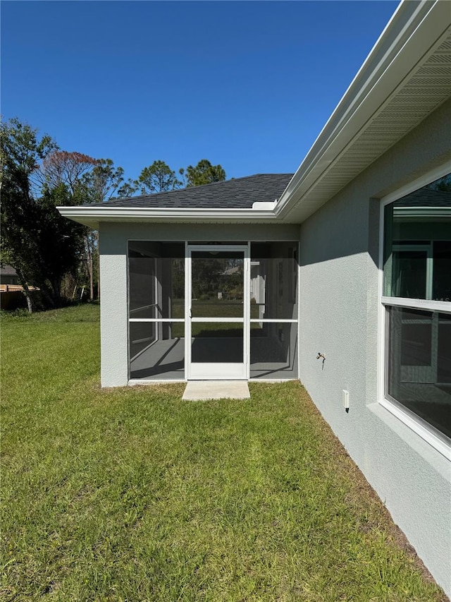 back of property featuring stucco siding, a shingled roof, a yard, and a sunroom