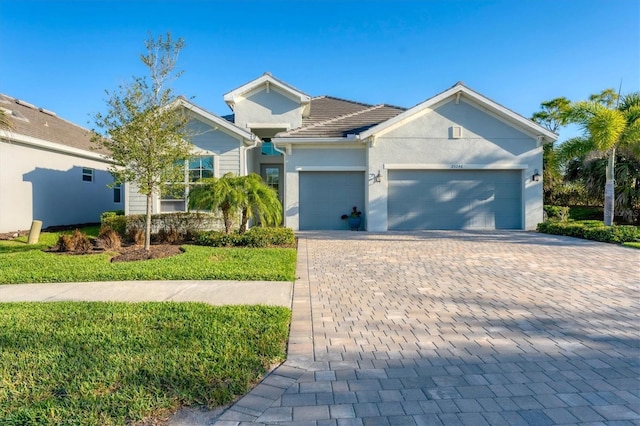 ranch-style home featuring decorative driveway, a front lawn, an attached garage, and stucco siding