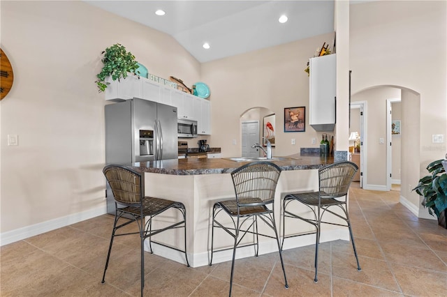 kitchen featuring arched walkways, high vaulted ceiling, appliances with stainless steel finishes, and a breakfast bar