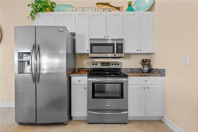 kitchen with stainless steel appliances, dark stone counters, light tile patterned flooring, white cabinets, and baseboards