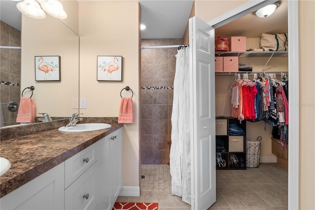 full bathroom featuring a sink, tile patterned flooring, double vanity, tiled shower, and a spacious closet