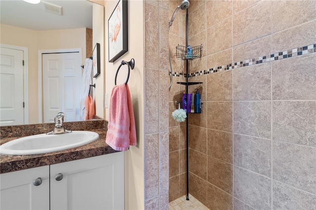 bathroom with visible vents, tiled shower, and vanity