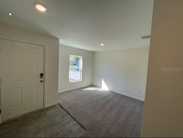 empty room featuring dark wood finished floors, baseboards, visible vents, and a textured ceiling