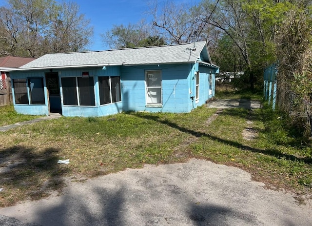 rear view of property featuring concrete block siding, a yard, a sunroom, and a shingled roof