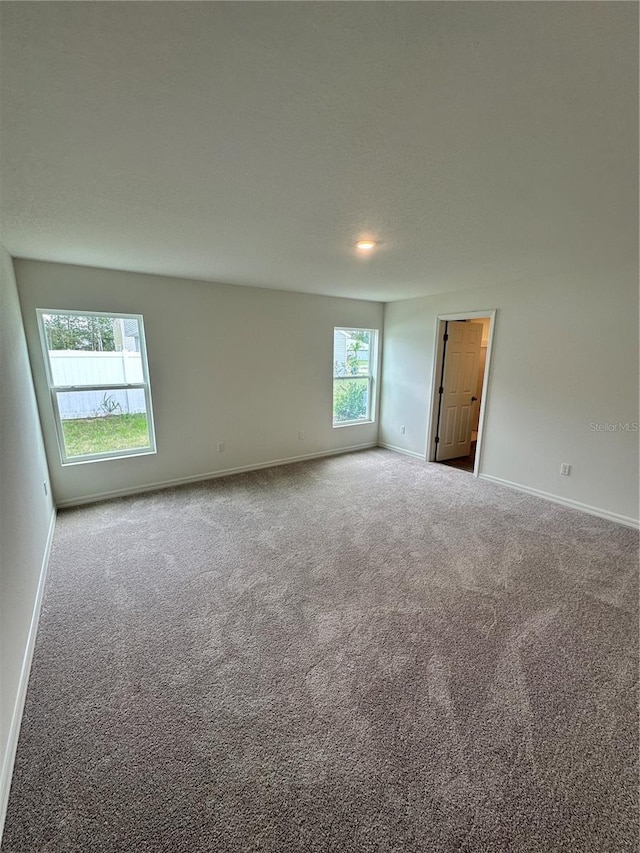 carpeted spare room featuring a textured ceiling and baseboards