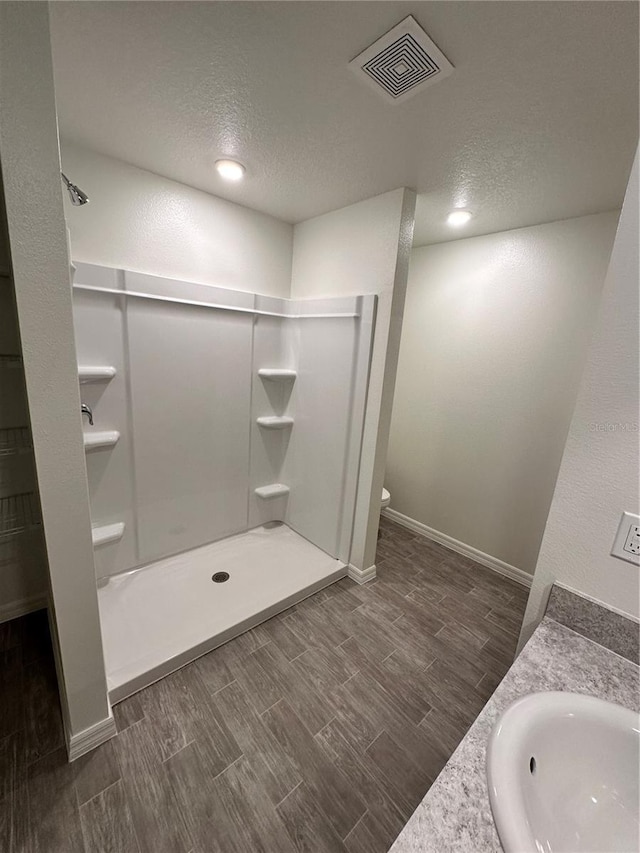 bathroom with visible vents, wood finish floors, a sink, a shower stall, and a textured ceiling