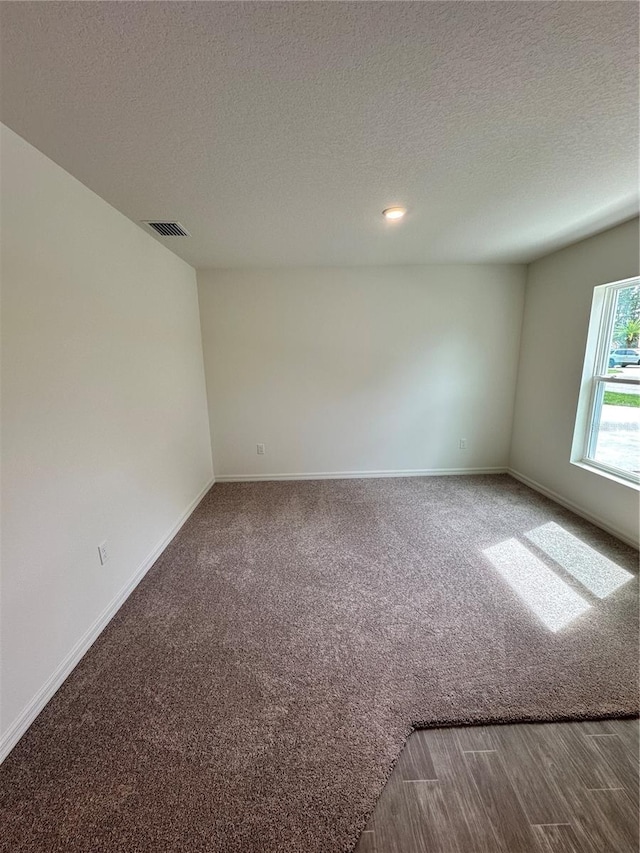 unfurnished room featuring visible vents, baseboards, a textured ceiling, and carpet
