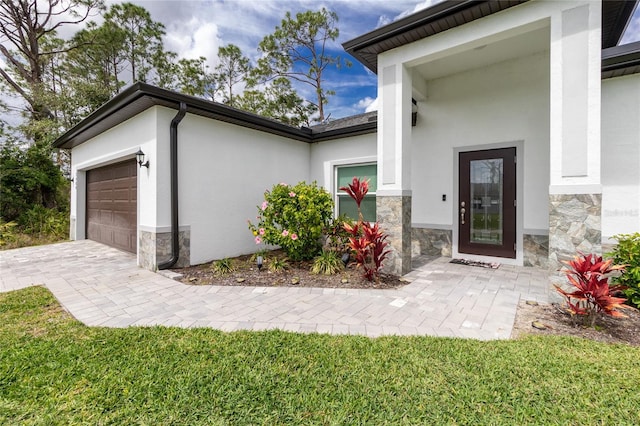 view of exterior entry featuring stucco siding, stone siding, an attached garage, and decorative driveway