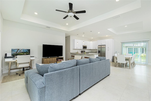 living room with visible vents, a ceiling fan, a tray ceiling, recessed lighting, and baseboards