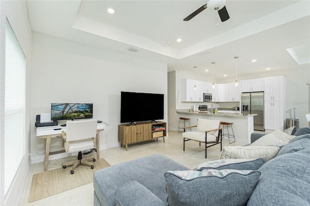 living room with visible vents, recessed lighting, a raised ceiling, and baseboards