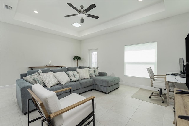 living room featuring light tile patterned floors, visible vents, baseboards, and a tray ceiling