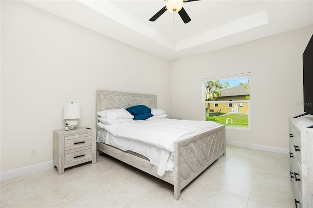 bedroom with light tile patterned flooring, a ceiling fan, a raised ceiling, and baseboards