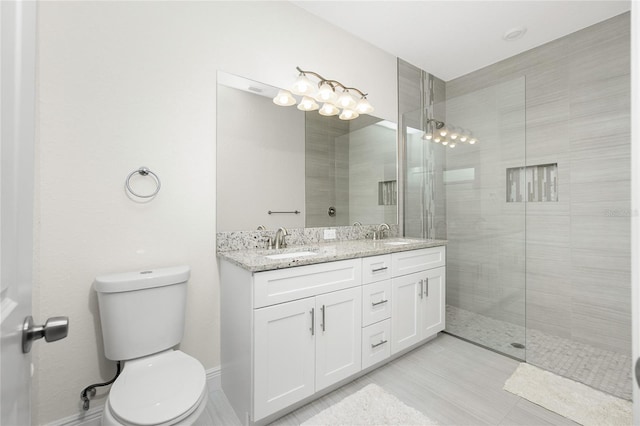 full bathroom featuring double vanity, tiled shower, toilet, and a sink