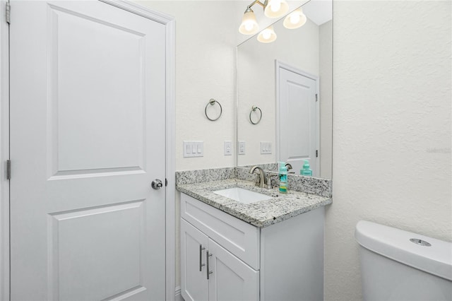 bathroom with toilet, vanity, and a textured wall