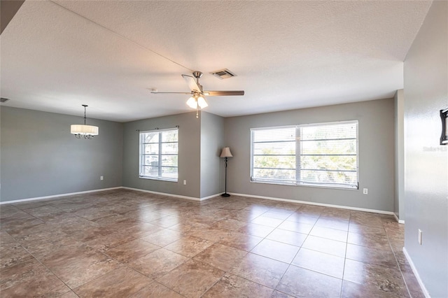 empty room featuring visible vents, ceiling fan with notable chandelier, a textured ceiling, and baseboards