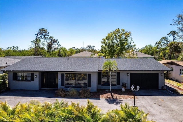 ranch-style house with aphalt driveway, a garage, a shingled roof, and stucco siding