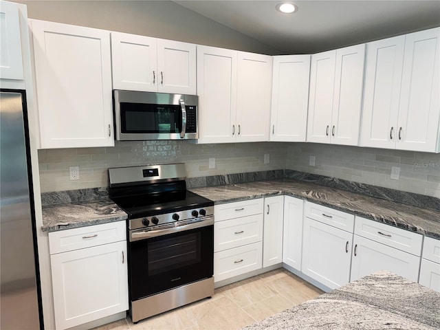 kitchen featuring dark stone countertops, backsplash, stainless steel appliances, white cabinets, and lofted ceiling