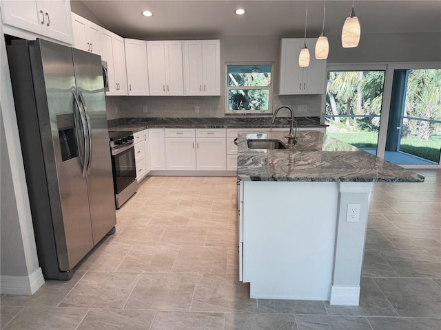 kitchen featuring a center island with sink, a sink, tasteful backsplash, dark stone counters, and appliances with stainless steel finishes