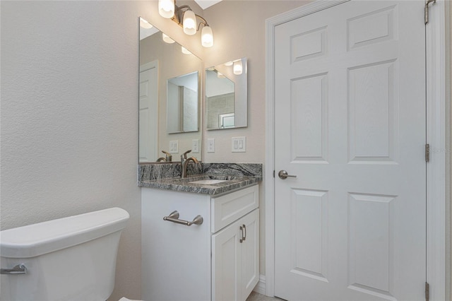 bathroom with vanity, toilet, and a textured wall