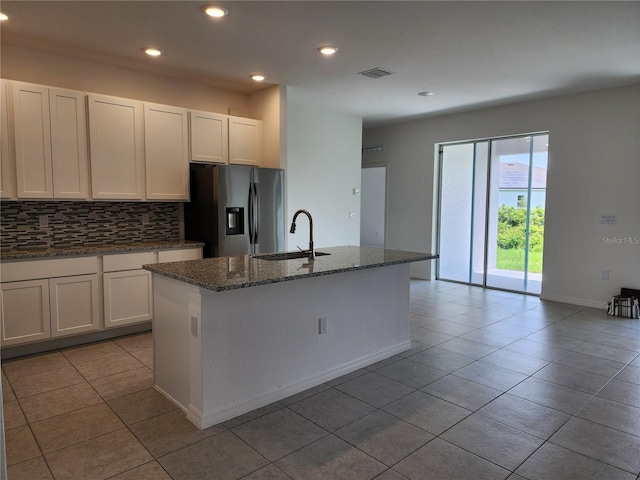 kitchen with visible vents, decorative backsplash, dark stone countertops, stainless steel refrigerator with ice dispenser, and a sink