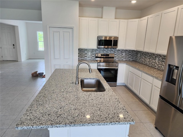 kitchen with a sink, light stone counters, backsplash, appliances with stainless steel finishes, and light tile patterned floors