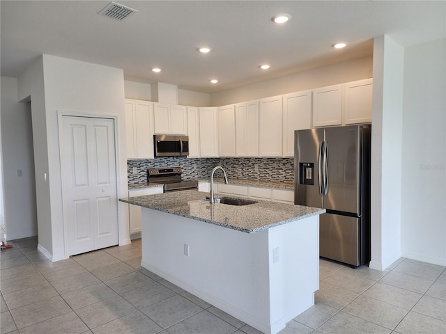 kitchen with an island with sink, a sink, backsplash, stainless steel appliances, and light stone countertops