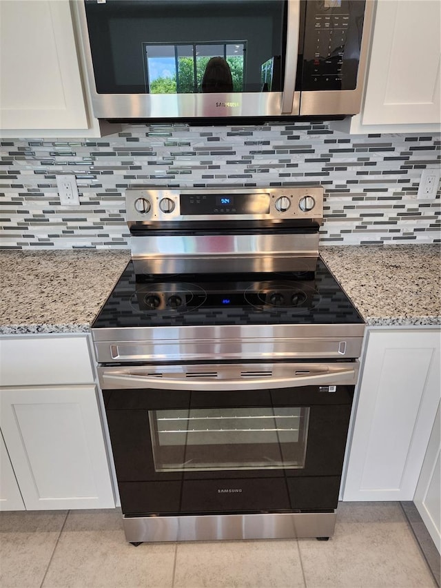 interior details with decorative backsplash, appliances with stainless steel finishes, white cabinetry, and light stone countertops