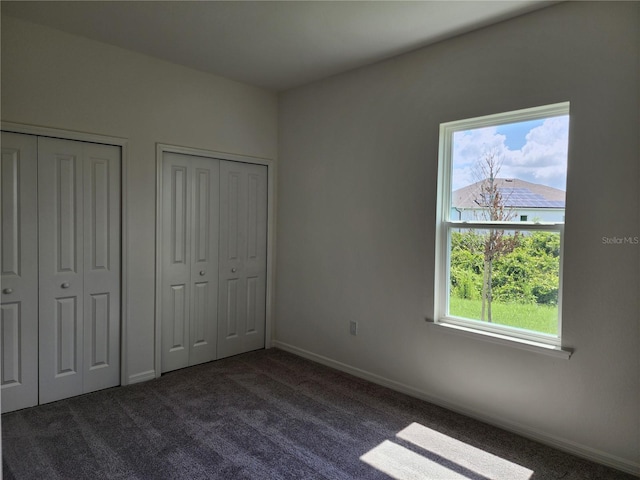 unfurnished bedroom featuring baseboards, multiple closets, and dark carpet