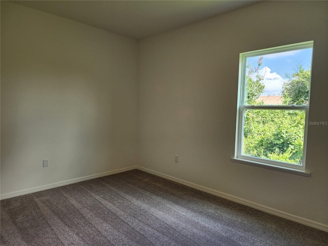 empty room featuring baseboards and dark colored carpet