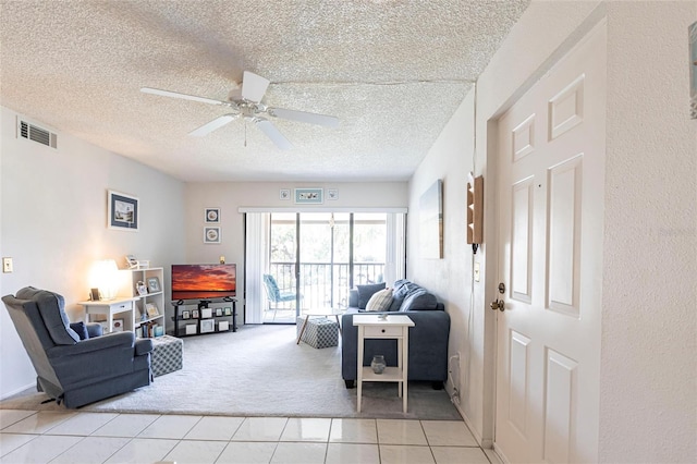 living area featuring a textured ceiling, light tile patterned flooring, light colored carpet, and ceiling fan