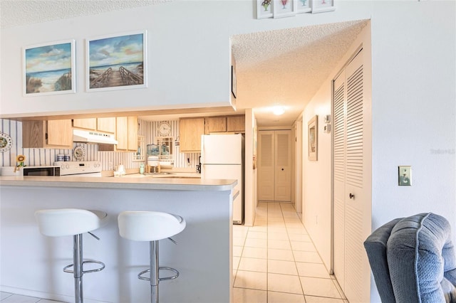 kitchen with under cabinet range hood, light countertops, light tile patterned floors, freestanding refrigerator, and a textured ceiling