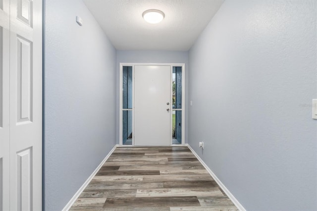 doorway to outside with baseboards, a textured ceiling, and wood finished floors