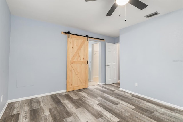 empty room with visible vents, baseboards, ceiling fan, a barn door, and wood finished floors