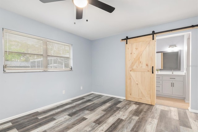 empty room featuring baseboards, a barn door, wood finished floors, a ceiling fan, and a sink