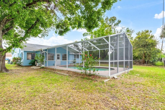 rear view of house featuring fence, a lanai, a lawn, stucco siding, and an outdoor pool