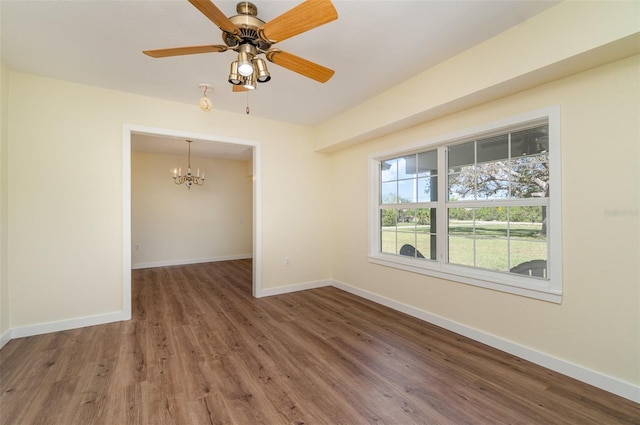 empty room with ceiling fan with notable chandelier, baseboards, and wood finished floors