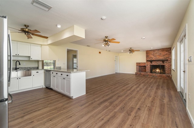 kitchen featuring visible vents, a peninsula, a fireplace, white cabinetry, and open floor plan