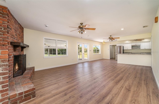 unfurnished living room featuring a ceiling fan, wood finished floors, visible vents, baseboards, and a fireplace