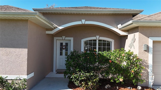 doorway to property featuring stucco siding and roof with shingles