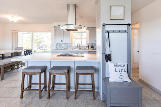 kitchen featuring a breakfast bar, a sink, island exhaust hood, tasteful backsplash, and black electric stovetop