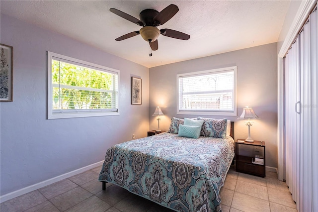 tiled bedroom with baseboards, a textured ceiling, and ceiling fan