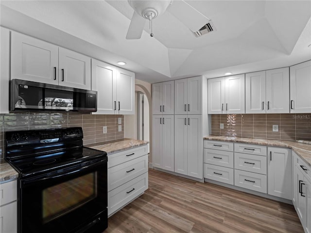 kitchen with black electric range oven, stainless steel microwave, white cabinetry, arched walkways, and light wood-style floors