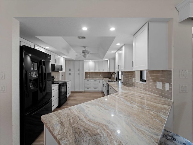 kitchen with light stone countertops, backsplash, black appliances, and white cabinetry