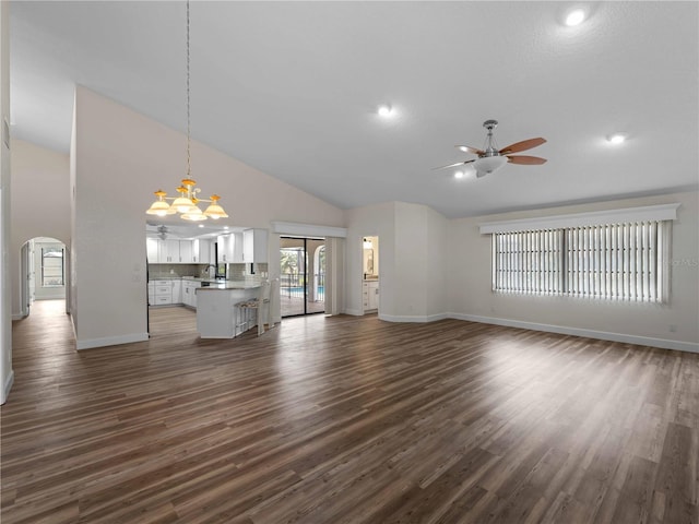 unfurnished living room featuring high vaulted ceiling, arched walkways, dark wood-style flooring, a sink, and ceiling fan