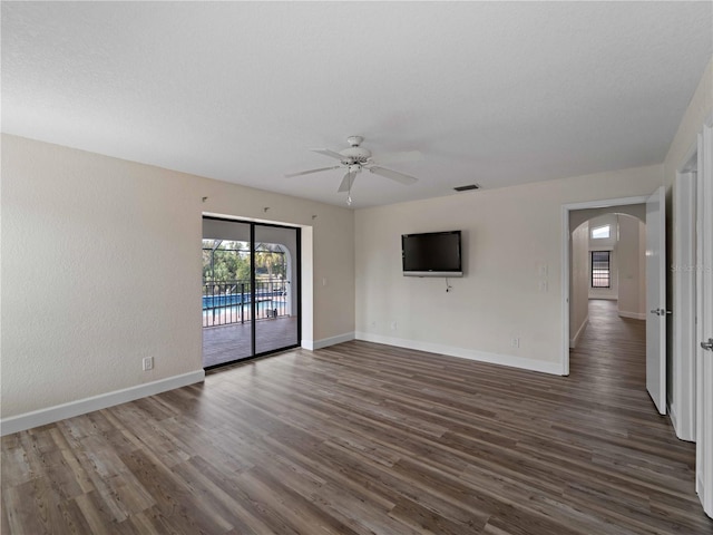 unfurnished living room with visible vents, dark wood-style floors, arched walkways, and baseboards