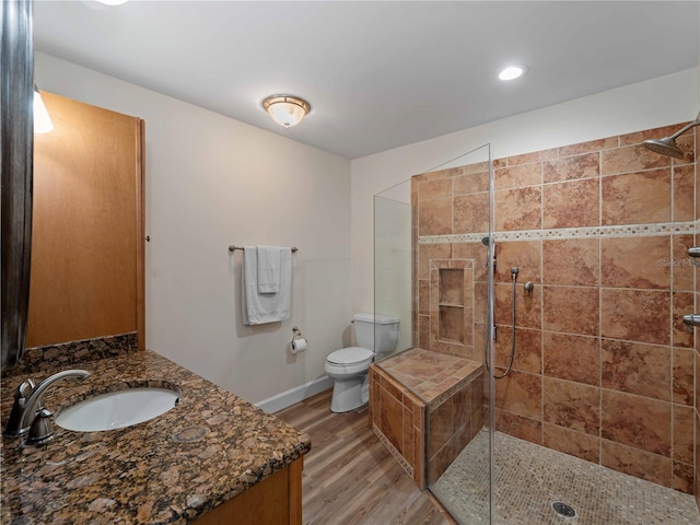 bathroom with baseboards, toilet, a tile shower, wood finished floors, and vanity